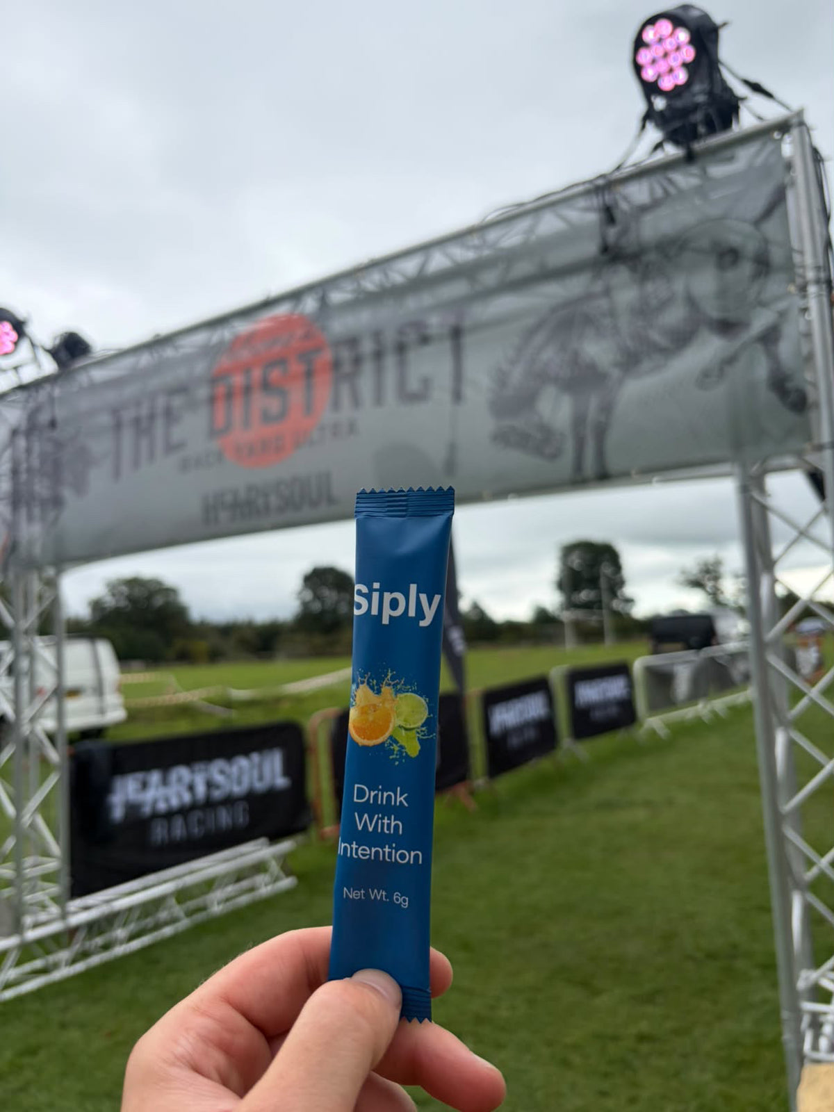 A Siply electrolyte sachet held up at a running race start line